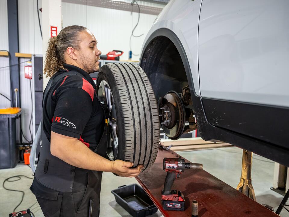 Monteur van FZ Auto's haalt een wiel van de auto, met remschijf en ophanging in beeld
