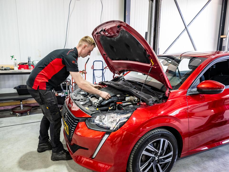 Monteur van FZ Auto's werkt onder de motorkap van een rode auto in Peize